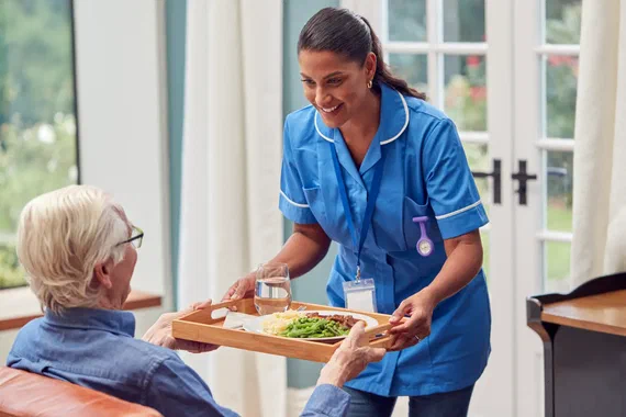 Pflegerin reicht einer Seniorin ein Tablett mit Essen