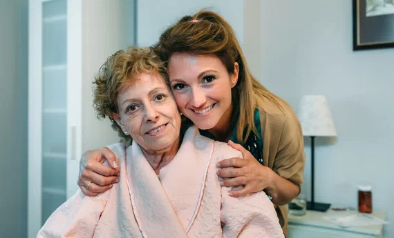 Pflegerin umarmt eine glückliche Seniorin im Altenheim